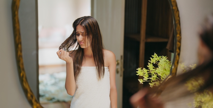 Zmartwiona kobieta w ręczniku w łazience ogląda swoje suche, matowe włosy