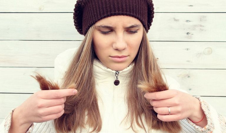 Młoda dziewczyna w zimie w czapce ogląda swoje suche, długie włosy